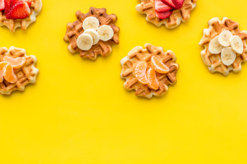 homemade Belgian waffles with fruit topings on yellow background top view copy space