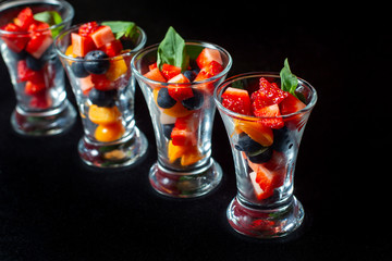Four cups with sliced strawberries and blueberries.