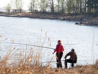 Two people are fishing on the river bank.