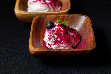 Wooden plate of blueberry ice cream with fresh berries on black table.