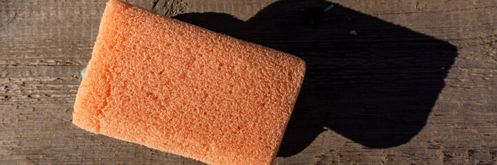 old pink cleaning sponge lies on a wooden surface.