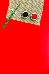 asian cuisine set with bamboo sticks, soy sauce and ginger for sushi and maki on red background top view mock up