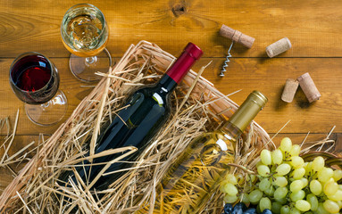 Two bottles, glasses of wine, bunches of grapes on wooden table.
