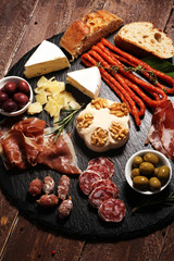 Cutting board with prosciutto, salami, cheese,bread and olives on dark stone background