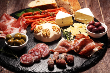 Cutting board with prosciutto, salami, cheese,bread and olives on dark stone background