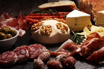 Cutting board with prosciutto, salami, cheese,bread and olives on dark stone background