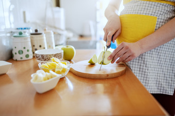 Obraz na płótnie Canvas Close up of pregnant Caucasian woman in apron cutting green apple in kitchen.