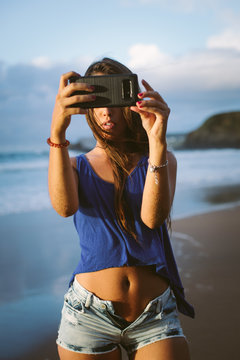 Young woman taking a selfie photo with her smartphone camera on summer vacation at the beach.	