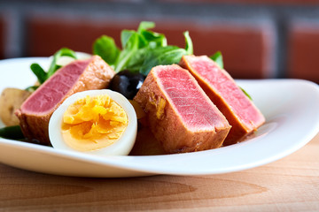 Nicoise salad with grilled tuna and boiled egg on a wooden background, close-up