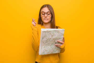 Fototapeta premium Young pretty caucasian woman crossing fingers for having luck. She is holding a map.