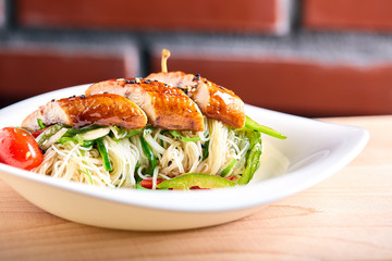 Asian noodles of funchoz with chopped vegetables and marinated chicken. Wooden background, close-up.
