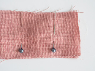 Sewing pins in linen fabric on white background, sewing pin use for attaching fabric together temporarily before sewing it with hand or sewing machine for the strong permanent stitch.