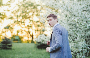 Naklejka na ściany i meble portrait of a fashionable handsome groom in a suit at sunset