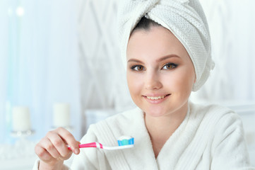 Portrait of beautiful young woman with towel on her head brushing teeth in bathroom