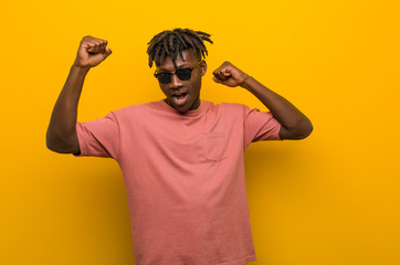 Fototapeta premium Young casual black man wearing sunglasses celebrating a special day, jumps and raising arms with energy.