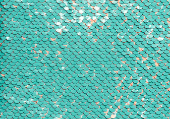 Sequin fabric background. Close-up shot of glittery blue or aquamarine colored sequins texture with coral dots