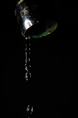 Faucet leaking water to black background. Macro detail of drop of water being wasted