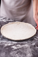 young woman in a gray aprong prepares a pepperoni pizza