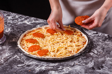 young woman in a gray aprong prepares a pepperoni pizza