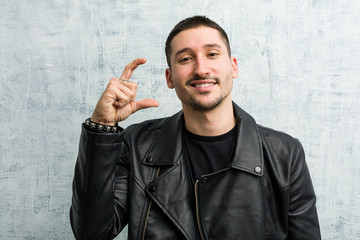 Young rocker man holding something little with forefingers, smiling and confident.