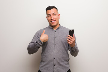 Young latin man holding a phone surprised, feels successful and prosperous