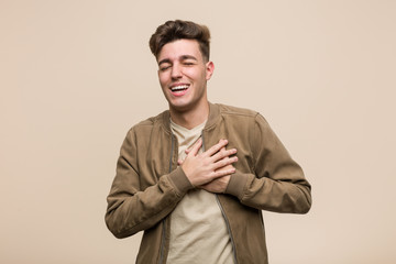 Young caucasian man wearing a brown jacket laughing keeping hands on heart, concept of happiness.