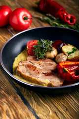 Grilled pork steak with vegetables in a pan. Dark wooden background, close-up