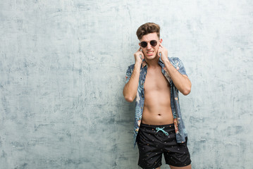 Fototapeta na wymiar Young caucasian man wearing a swimsuit covering ears with his hands.