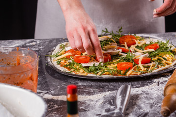 young woman in a gray aprong prepares a vegetarian pizza