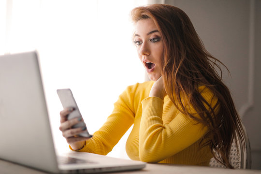Pretty young woman looks surprised while checking her smartphone.