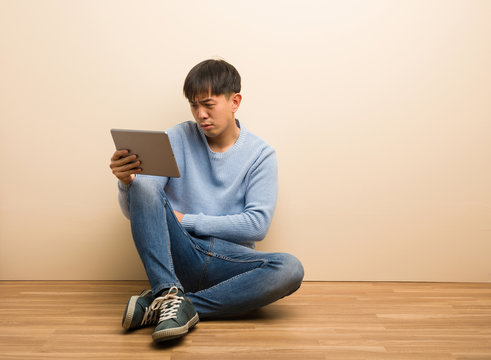 Young chinese man sitting using his tablet crossing arms relaxed