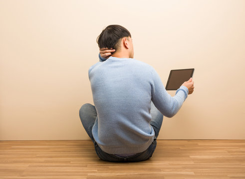 Young Chinese Man Sitting Using His Tablet From Behind Thinking About Something