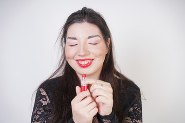 Asian happy woman paints her lips with lipstick on white studio background. Wrong try to do good self make up. Adult girl is learning to paint her face.