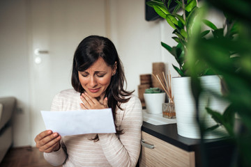 Woman crying over received letter, at home.