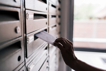Inserting letter into a building metal mailbox, close-up.