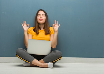 Young woman sitting on the floor with a laptop performing yoga
