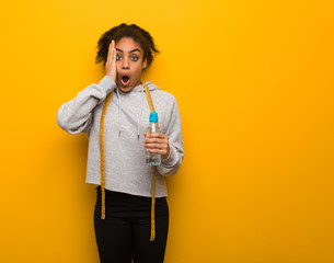 Young fitness black woman surprised and shocked.Holding a water bottle.