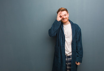 Young redhead man in pajama confident doing ok gesture on eye