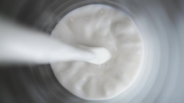 Top view of milk being poured in a glass on dark color table, close up of pouring milk on black background, slow motion