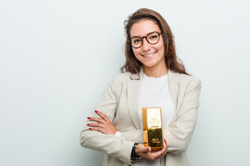 Young european business woman holding a gold ingot smiling confident with crossed arms.