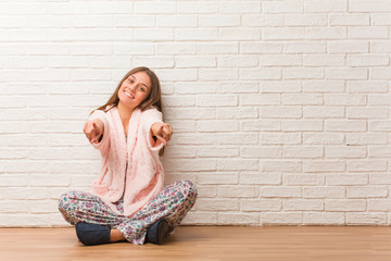 Young woman wearing pajama cheerful and smiling pointing to front