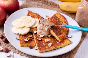 Pancakes with bananas, nuts, peanut butter on a wooden background