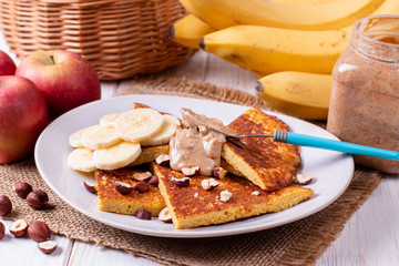 Pancakes with bananas, nuts, peanut butter on a wooden background