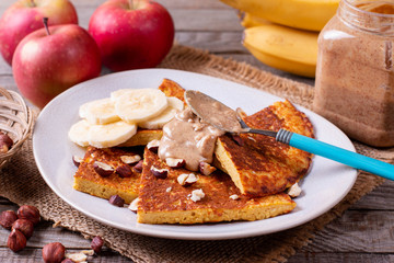 Pancakes with bananas, nuts, peanut butter on a wooden background
