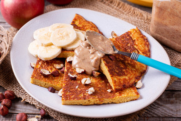 Pancakes with bananas, nuts, peanut butter on a wooden background