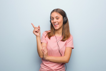 Young pretty caucasian woman pointing to the side with finger. She is listening to music with headphones.