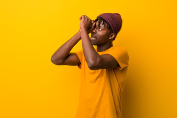 Young black man wearing rastas over yellow background looking far away keeping him hand on forehead.