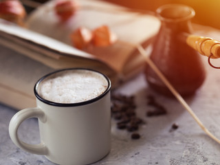 Milk coffee boiled in cezve, old book on gray background
