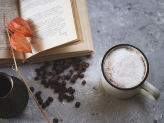 Milk coffee boiled in cezve, old book on gray background