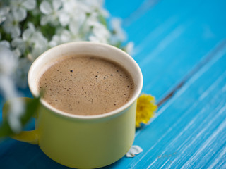 Spring coffee . Yellow Cup on blue background and cherry blossoms